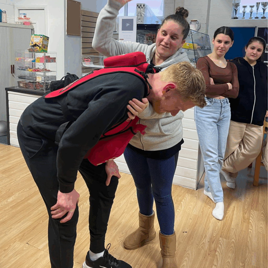 Bellstone Training participants practicing the Heimlich maneuver using a choking rescue vest during a first aid training session.